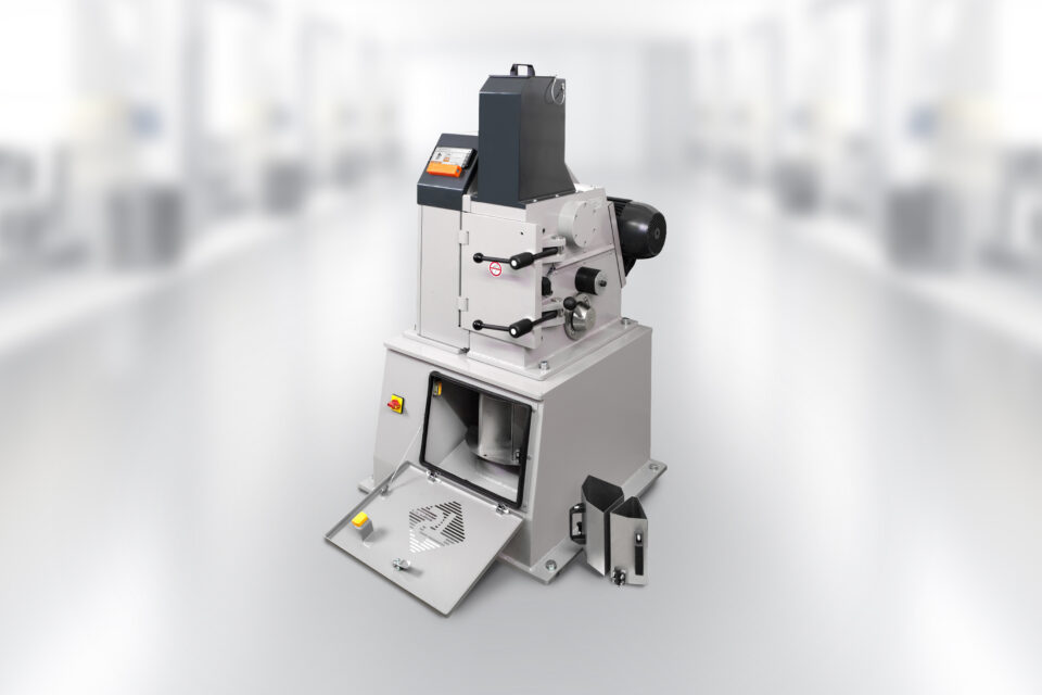 Single-toggle crusher / jaw crusher EB150x100 TL in the laboratory. The device's grinding chamber is open, 2 sub-units are next to the device. The smartphone with app control is switched on and ready for operation