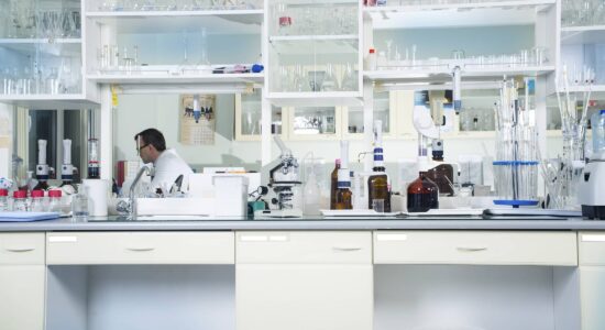 View of a laboratory. Various pieces of equipment can be seen in the foreground, with a laboratory employee sitting at the back